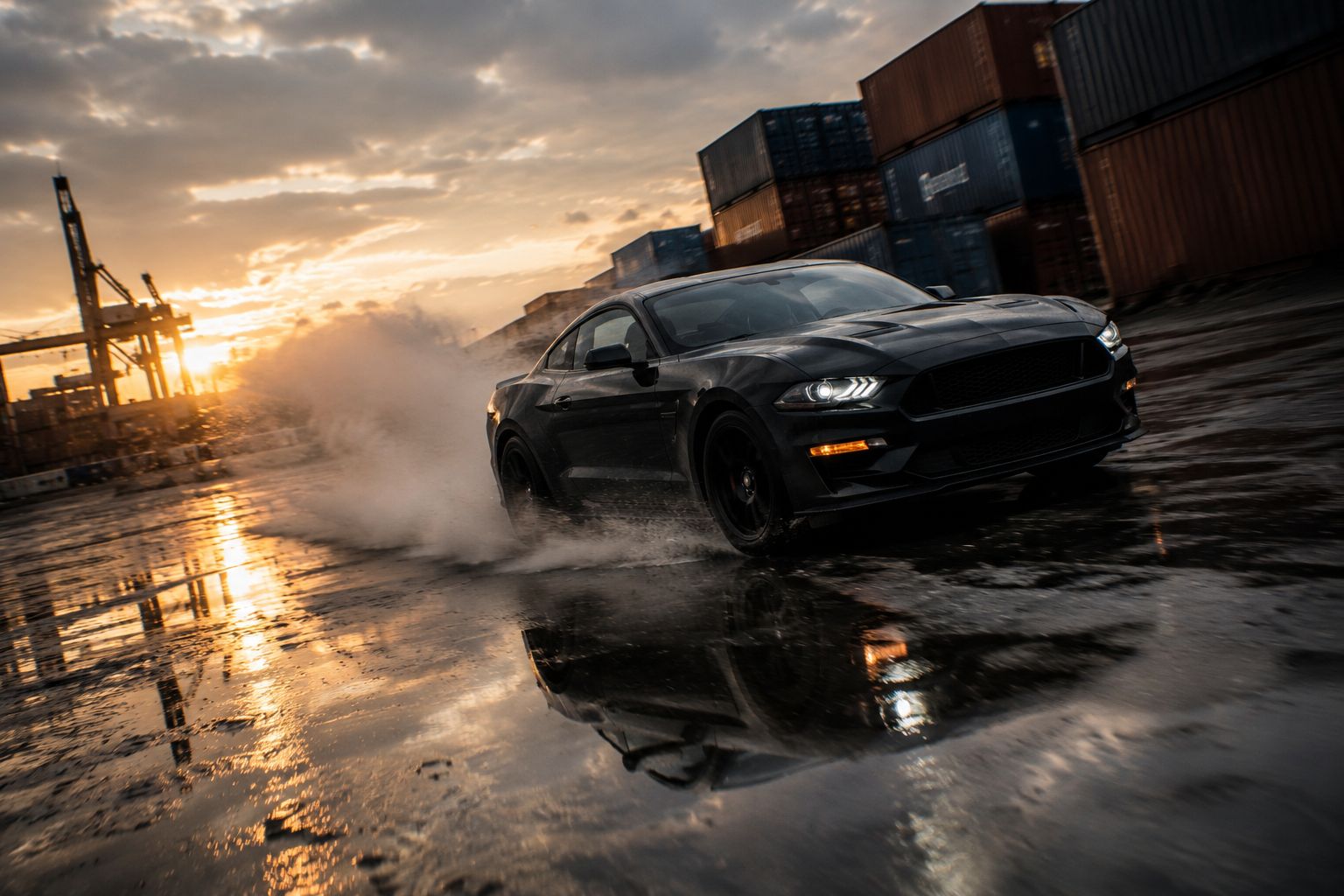 Black muscle car drifting at a container port at sunset